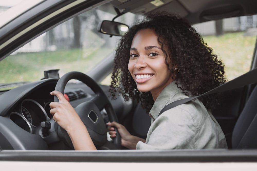 Mulher com mãos no voltante, dentro de um carro